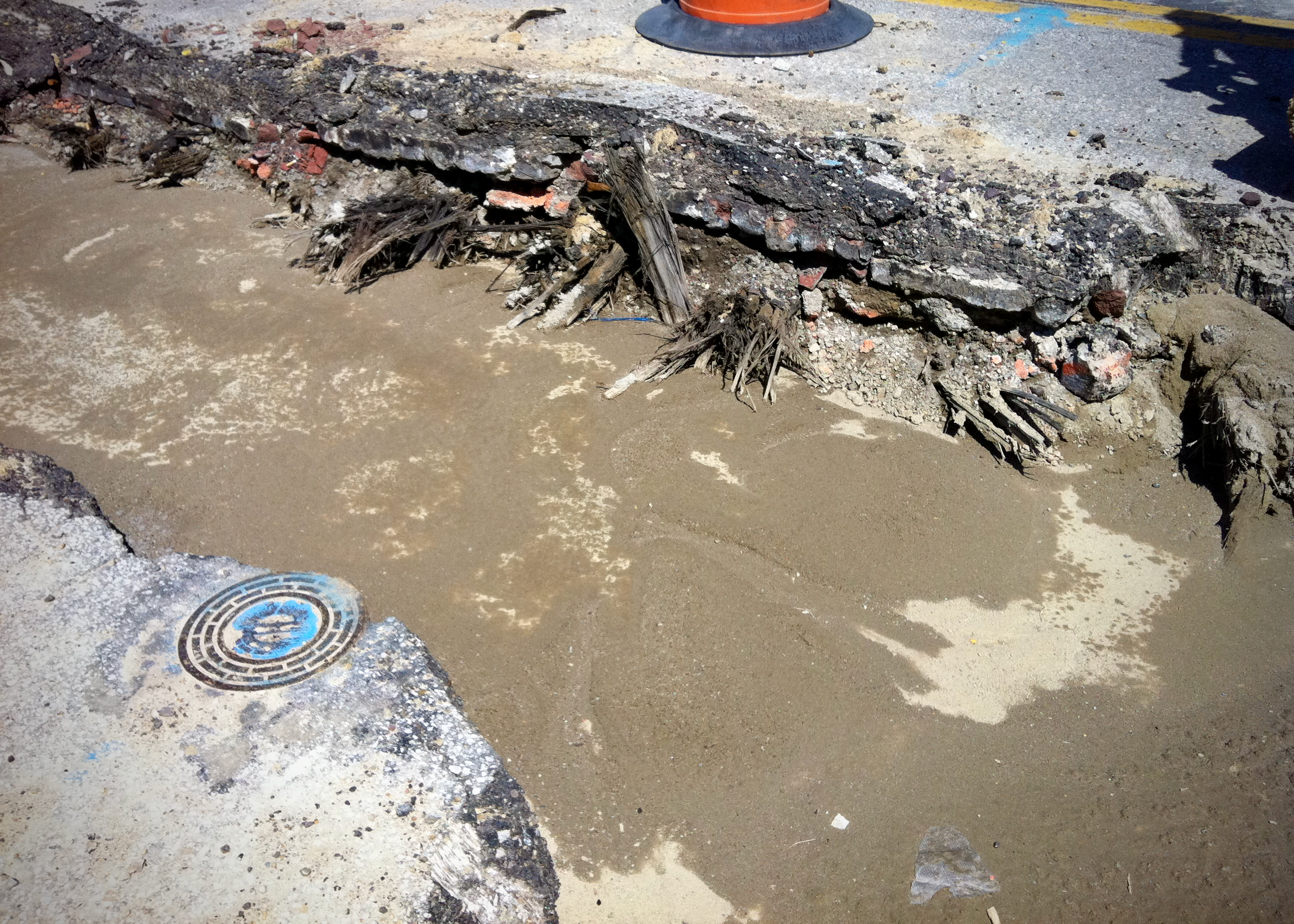 Exposed streetcar line remnants embedded in crumbling pavement and brick layers, with wood fragments protruding from a partially excavated roadbed.